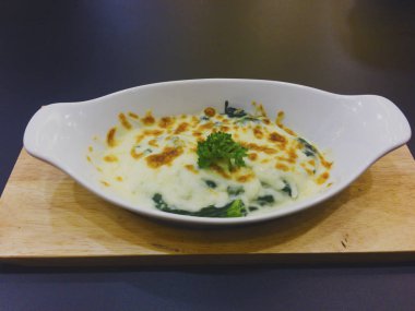 Peynirli fırında ıspanak ahşap tepsi üzerinde beyaz kase mevcuttur maydanoz yaprakları ile süslüdür.