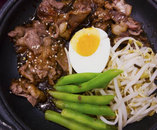 Japaneses 的食物 用酱油炒牛肉 在热锅上 上面有白色的芝麻籽 边菜由煮沸的蛋 豆芽和油炸的豆棍子组成 — 图库照片