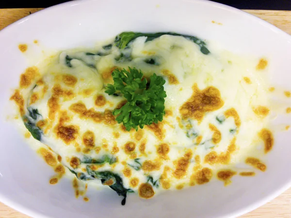 Peynirli fırında ıspanak ahşap tepsi üzerinde beyaz kase mevcuttur maydanoz yaprakları ile süslüdür.