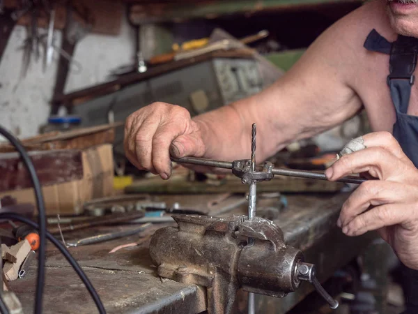 Äldre man i harnees vid hem workshop. Stäng upp syn på processen för skruv gängsvarvning. Arbetare sitter hemma workbench och att göra gängskärning. Suddig bakgrund, mjuk selektivt fokus. — Stockfoto