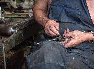 Atölyesinde çalışan adam, ellerinde yakın çekim. Arka plan bulanık, yumuşak seçici odak. Yaşlı bir adam iş işlemi sırasında fotoğraflandı. Tezgah oturma ve el aletleri ile çalışan adam.