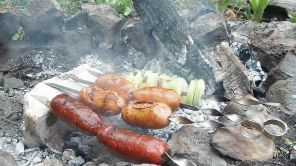 Salsicce e spiedini di cipolle in giardino privato. Quattro spiedini con salsicce e grigliate di cipolle con braci calde, vista da vicino. Legna da ardere fumante in camino pavimentato con pietre fuliginose . — Video Stock