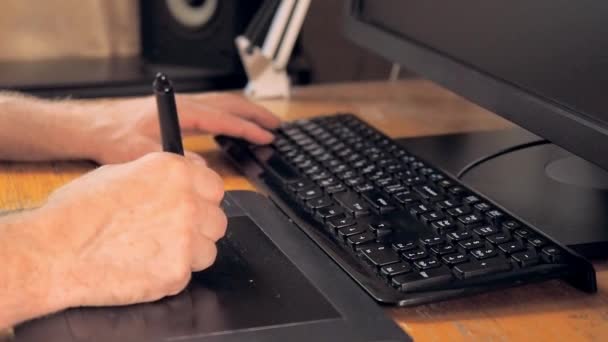 Equipment for graphic design. Touch screen pen, digital tablet, black keyboard and computer monitor. Close up on human hands drawing on tablet computer. Blurred background, soft selective focus. — Stock Video