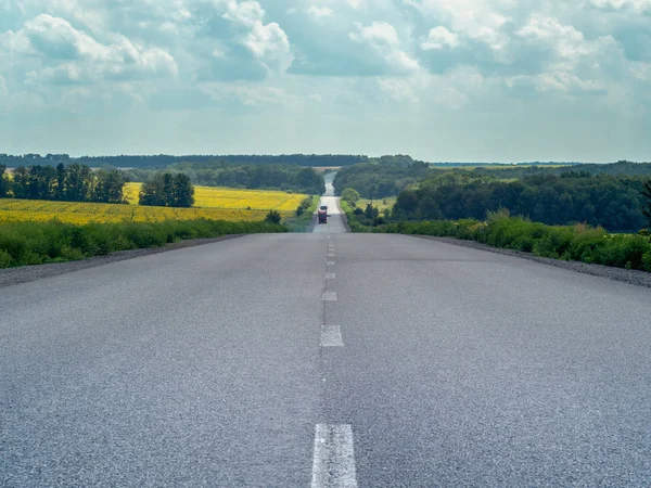 Country asphalt road disappearing on the horizon. Sky covered with white and grey clouds. Landscape of empty asphalt highway and rural area with green trees. Blurred background. Soft selective focus. — Stock Photo, Image