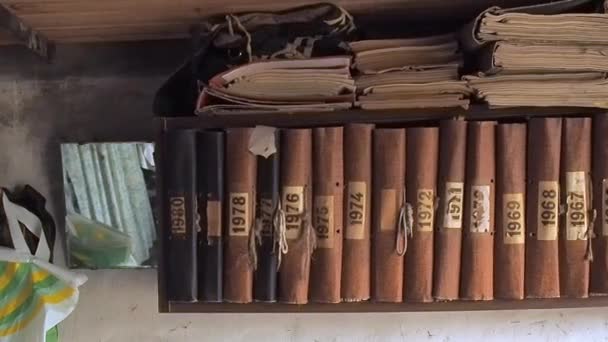 Viejos libros marrones en el estante, vista de cerca. Cámara moviéndose a lo largo de la estantería que cuelga en la pared del cobertizo. Libros antiguos de pie en fila en un estante de madera . — Vídeos de Stock