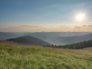 Yükselen güneş karanlık dağ aralıkları yukarıda. Karpatlar Dağları Ağustos, Batı Ukrayna. Otlak sabahın erken saatlerinde. Yaz adlı Ukraynalı doğa manzara. Mavi gökyüzü bulutlu. Arka plan bulanık.