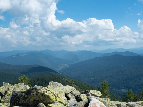 Paisaje de las montañas de los Cárpatos en verano, oeste de Ucrania. Cielo azul con gran cúmulo blanco. Valle entre verdes laderas cubiertas de denso bosque de abetos. Montón de piedras grises. Fondo borroso . — Foto de Stock