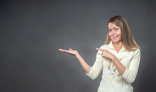 Donna sorridente si tiene per mano e felice di presentare copyspace. GIrl mostrando a qualcosa qualche prodotto, spazio palce vuoto per slogan, annunci di prodotti, messaggio di testo. Isolato su sfondo grigio — Foto Stock