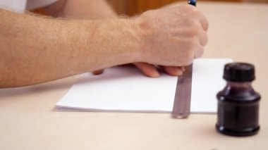 Cetvel ve fırça kalemi ile üzerine beyaz boş bir çizgi çekerek el mans. Yakın çekim. Yan görünümü. Tasarımcılar çalışma alanı üzerinde görüntüleme. Kaligrafi yazı için hazırlanıyor. Arka plan bulanık. İnkpot bej masa üzerinde.