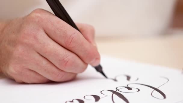 Calligraphe dessinant des lettres à blanc blanc. Plan rapproché. Vue de face. Lettrage calligraphique. Les hommes écrivent à blanc. Designer au travail. Mise au point sélective. Fond flou .