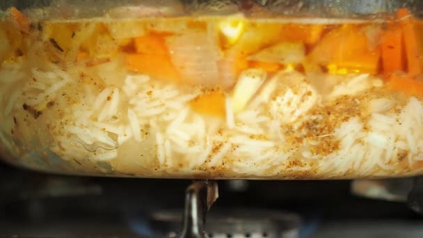 Βραστό πιλάφι σε γυάλινο δοχείο βρασμένο σε ένα καυστήρα αερίου στη σόμπα. Προβολή με μεγέθυνση. Ρύζι με καρότα, σκόρδο, κρεμμύδι και κρέας. Μαγείρεμα των τροφίμων, το ρύζι κουάκερ με λαχανικά και κρέας. — Αρχείο Βίντεο