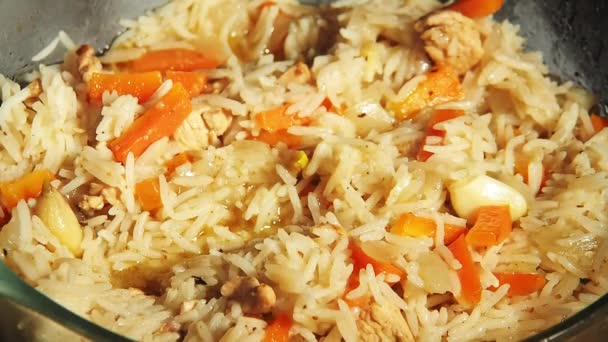 Pilaf bollente in padella di vetro, vista da vicino. Il riso con carote, aglio e carne lentamente bolle. Cottura di cibo, porridge di riso con verdure e carne — Video Stock