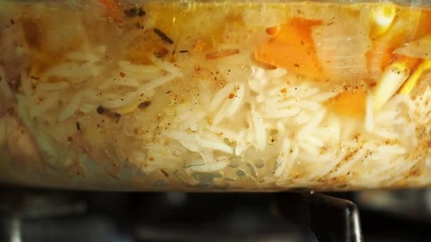 Pilaf bouillant dans un pot en verre. Vue rapprochée. Nourriture asiatique nationale. Le riz aux carottes, à l'ail, à l'oignon et aux furoncles de viande est sur le feu. Cuisson des aliments, bouillie de riz aux légumes et viande . — Video