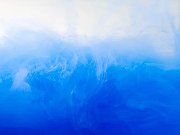 Une goutte de peinture bleue se dissolvant dans l'eau, vue de près. Contexte abstrait. Nuages acryliques tourbillonnant dans le liquide. Ondes d'encre acrylique dans l'eau, motif abstrait. Peindre dans du liquide. Fond flou . — Photo