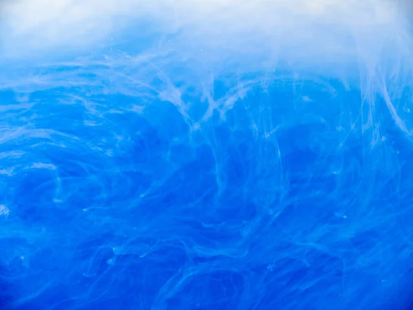 Синие акриловые чернила в жидкости, вид вблизи. Абстрактный фон. Краска растворяется в воде. Абстрактные голубые облака, кружащиеся в воде. Акриловые волны в жидком, абстрактном образце. Размытый фон . — стоковое фото