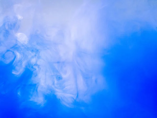 Movement of acrylic waves while dissolving into water, close up view. Abstract background. Drop of blue paint dissolved into liquid. Blue and white ink clouds swirling in water. Blurred background. — Stock fotografie