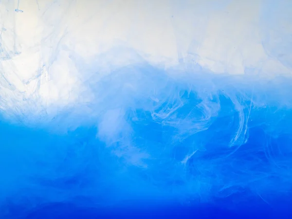 Waves of blue acrylic paint in water, close up view. Abstract background. Acrylic clouds swirling in liquid. Ink dissolving into water, abstract pattern. Drop of paint in liquid. Blurred background.