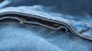 Kot pantolon. Metal düğmeler, kumaş dokusu ve kaba iplikler ile dikişler yakın çekim. Kot pantolon lar masanın üzerinde yatıyordu. Dolly kayar makro çekim. Seçici yumuşak odaklama.