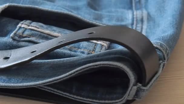 Blue denim jeans laying on the table. Macro dolly shot. Selective soft focus. Camera moving along leather belt. Clothing for everyday wearing. Blue trousers, close view. — Stock Video