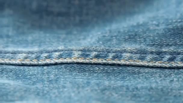 Blue jeans laying on the table. Macro dolly shot. Selective soft focus. Camera moving along side seam of jeans. Texture of denim, background from denim texture close up. — Stock Video