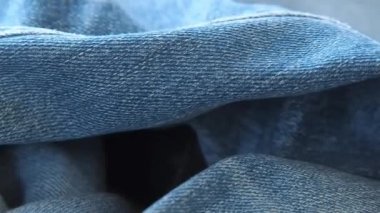 Kot pantolon lar masanın üzerinde yatıyordu, yakın çekim. Bulanık arka plan. Seçici yumuşak odak. Kamera sinek düğmesi ile buruşturulmuş kot boyunca hareket ediyor. Günlük giyim için giyim. Moda arka plan.