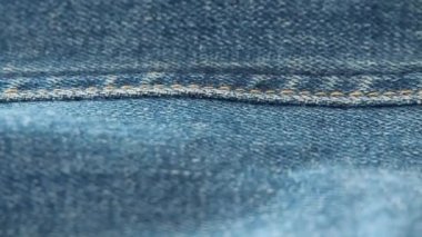 Kot pantolon dokusu, yakın çekim. Bulanık arka plan. Seçici yumuşak odak. Kamera kot dikiş boyunca hareket ediyor. Denim doku, duvar kağıtları ve moda afiş için arka plan.