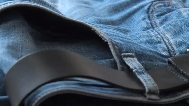 Jeans blu con cintura in pelle posata sul tavolo, colpo ravvicinato. Sfondo sfocato. Concentrazione selettiva morbida. Fotocamera in movimento lungo la cintura e tasche pantaloni anteriori. Sfondo per banner di moda e sfondi . — Video Stock