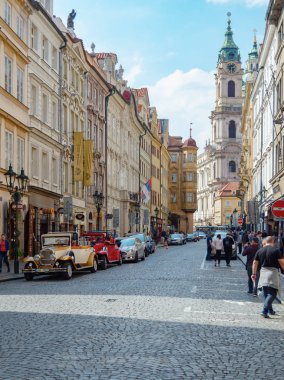 Prag, Çek Cumhuriyeti - Nisan 2019: Dar sokak yüksek saat kulesine iniyor. Yolda yürüyen bir sürü turist gri taşlarla döşendi. Prag'da Streen park vintage ve modern arabalar.