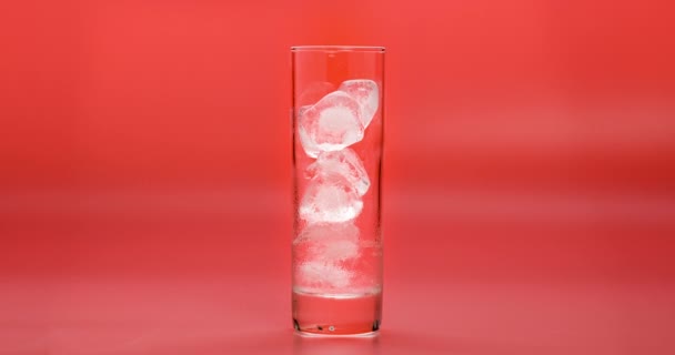 Lasso di tempo di sciogliere i cubetti di ghiaccio nel bicchiere da vicino sullo sfondo di corallo. Bicchiere di acqua fredda con vetro nebulizzato su sfondo rosa . — Video Stock