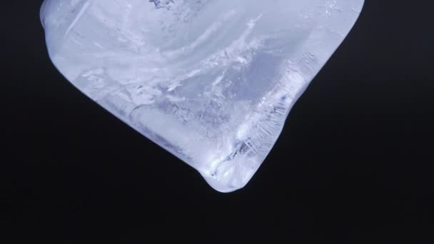 Makro video natáčení tání ledu kostky na černém pozadí. V reálném čase. Postřelen zblízka. Ledová kostka s kapkami padající vody. — Stock video