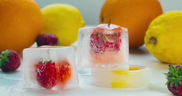 Tidsförlopp för smältande isbitar med frysta jordgubbar. Jordgubbar frusna i isbitar. Showcase av färgglada välsmakande frukt. Apelsiner, jordgubbar, citroner nära på vit bakgrund. — Stockvideo