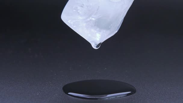 黒い背景に溶ける氷の立方体のマクロビデオ撮影。水滴が落ちて水たまりを形成します。リアルタイム処理。水滴が落ちるアイスキューブ — ストック動画