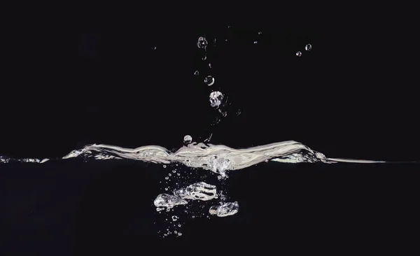 Goccia d'acqua fotografata mentre si fa spruzzare sulla superficie liquida, isolata su fondo nero, vista da vicino. Bolle d'acqua e superficie increspata. Immagine per la progettazione di sovrapposizioni, livello di modalità di miscelazione . — Foto Stock