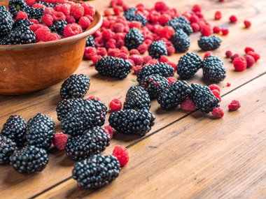 Kahverengi havza kırmızı ahududu ve siyah dut dolu, yakın görünümü. Taze olgun meyveler kahverengi masaya yığılmış. Ahşap masa dokusu. Seçici yumuşak odak. Bulanık arka plan.