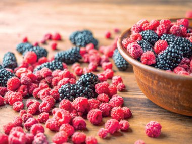 Kahverengi masada siyah dut ve kırmızı ahududu, yakından görünümü. Kahverengi kase kırmızı ve siyah çilek dolu. Meyve arka planı. Seçici yumuşak odak. Bulanık arka plan.
