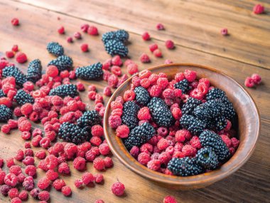 Kahverengi havza kırmızı ahududu ve siyah dut dolu, yakın görünümü. Kahverengi masada siyah ve kırmızı meyveler. Meyve arka planı. Seçici yumuşak odak. Bulanık arka plan.