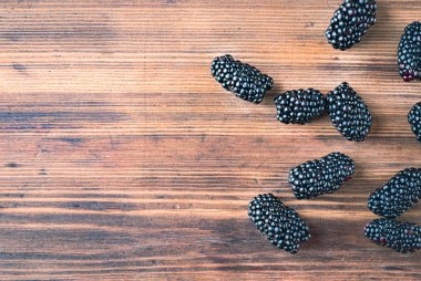 Kahverengi masanın üzerine yatan siyah dutlar, yakından görünümü. Ahşap masa dokusu. Ahşap masada sulu meyveler. Meyve arka plan.