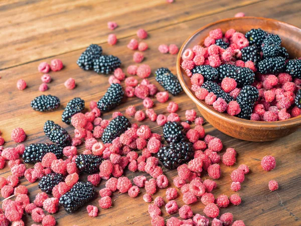 Kahverengi masaüzerinde yatan kırmızı ahududu ve siyah dut yakından görünümü. Kahverengi çanak kırmızı ve siyah çilek dolu. Meyve arka planı. Seçici yumuşak odak. Bulanık arka plan.