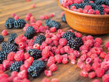 Siyah ve kırmızı meyveler kahverengi masa üzerinde döşeme, yakın görünümü. Kahverengi havza kırmızı ahududu ve kara dut dolu. Ahşap masa dokusu. Seçici yumuşak odak. Bulanık arka plan.