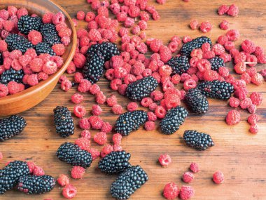 Olgun sulu meyveler kahverengi masa üzerinde döşeme, yakın görünümü. Kahverengi havza kırmızı ahududu ve kara dut dolu. Ahşap masa dokusu. Seçici yumuşak odak. Bulanık arka plan.