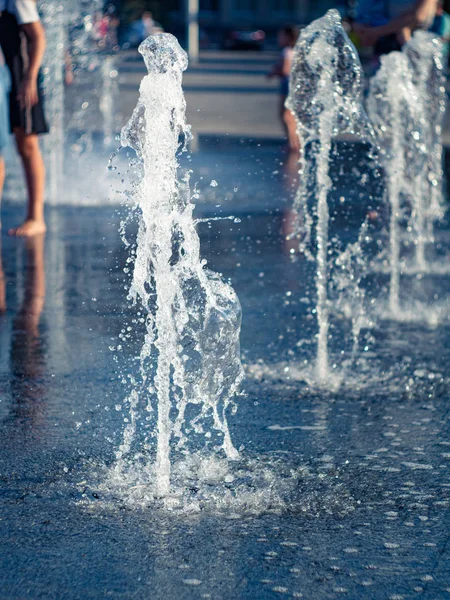Flujos de agua de fuente seca en la plaza de la ciudad, vista de cerca. Niños enfriándose entre aerosoles de agua. Fondo de paisaje urbano de verano. Enfoque suave selectivo. Fondo borroso . —  Fotos de Stock