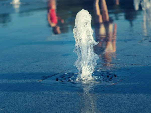 Corriente de agua de fuente seca que fluye fuera de la rejilla inoxidable, vista de cerca. Madre con el niño reflejándose en la superficie del agua. Plaza de verano. Enfoque suave selectivo. Fondo borroso . —  Fotos de Stock