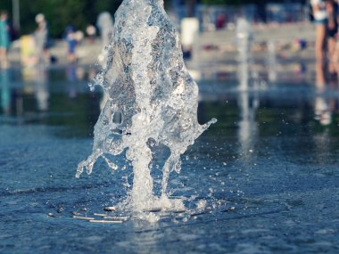 Kuru çeşme paslanmaz ızgara dışarı akan su akışı üzerinde görünümü kapatın. Fıskiyenin yanında soğuyor çocukları olan ebeveynler. Yaz şehir manzarası. Seçici yumuşak odak. Bulanık arka plan.