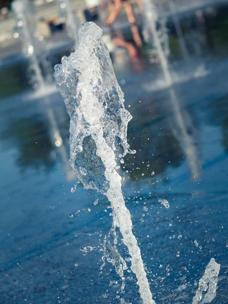 Dere ve su damlaları kare granit kaplama üzerine sıçrayan, görünümü kapatın. Çocuklar kuru çeşme nin yanında çıplak ayaklar. Yaz şehir manzarası. Seçici yumuşak odak. Bulanık arka plan.