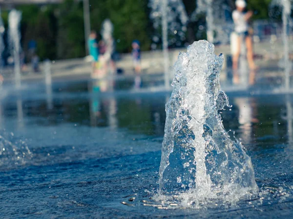 Kuru çeşmenin granit kaplamasına sıçrayan dikey su akışları, görünümü kapatın. Çeşmenin içinde soğutan çocuklar. Yaz şehir manzarası. Seçici yumuşak odak. Bulanık arka plan.