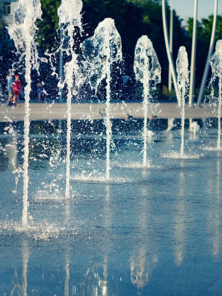 Крупним планом вид на водні потоки, що вириваються з неіржавної решітки. Сухий фонтан на головній площі міста. Діти ходять біля фонтану. Літній пейзаж. Вибірковий м'який фокус. Розмитий фон . — стокове фото