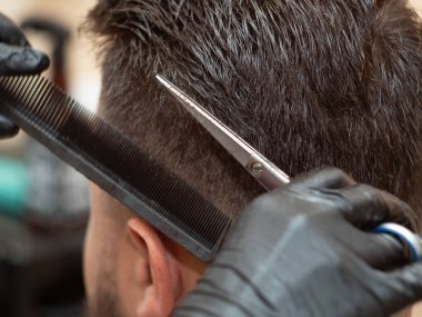 Stilistler siyah lastik eldivenler giyip saçlarını makas ve tarak ile kesiyorlar, manzarayı kapatıyorlar. Kuaför salonunda stilistlik yapıyor. Seçici yumuşak odaklanma. Bulanık arkaplan.