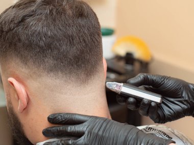 Müşteriler yakın kırpılmış, yakından görünümü ense. Kuaför makas ile saç kesme. Elleri siyah lastik eldivenler. Kuaför salonunun içi. Seçici yumuşak odak. Bulanık arka plan.