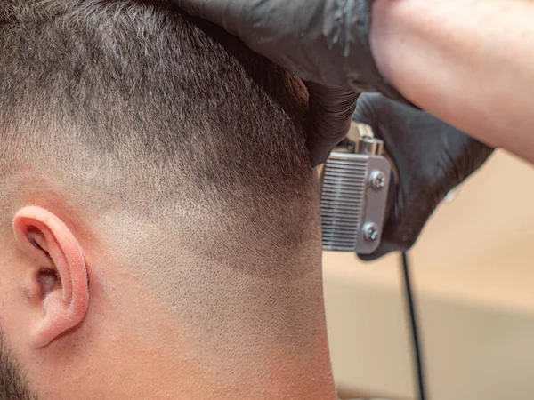 Kuaför makas ile çalışan, erkekler ense ve kulak, yakın. Ustalar siyah lastik eldivenler içinde elleri. Müşteriler yakın kırpılmış ense. Berber dükkanında fotoğraflandı. Seçici yumuşak odak. Bulanık arka plan.