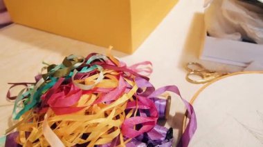Çok renkli şeritler ve çemberler kutuların ortasında masanın üzerinde yatıyor. Kadın elleri makara bantları koyar. Yakın çekim. Elle çekim efektleri ile hareketli kamera.
